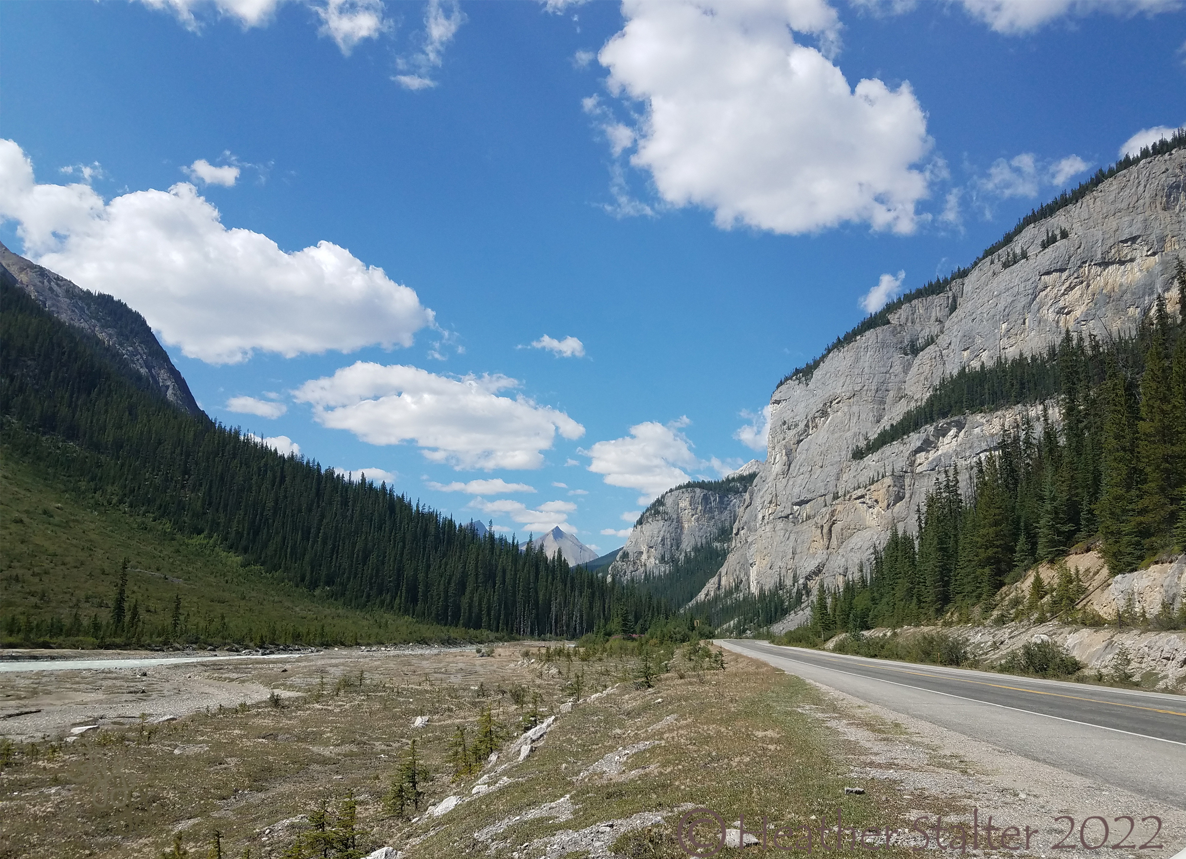 blue sky and clouds, with a road an mountains and trees