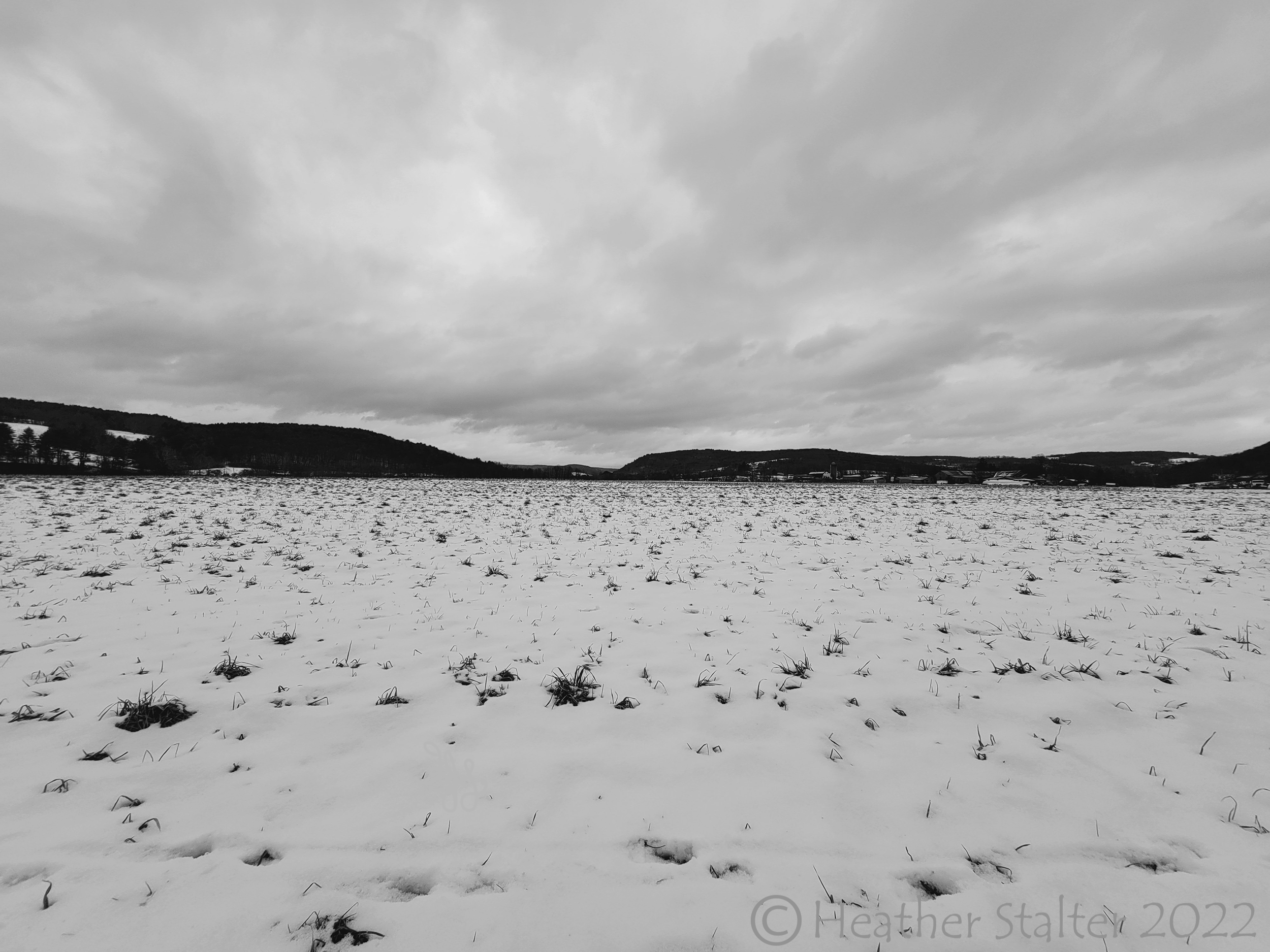 black and white of a stark landscape of field and sky with hills in distance