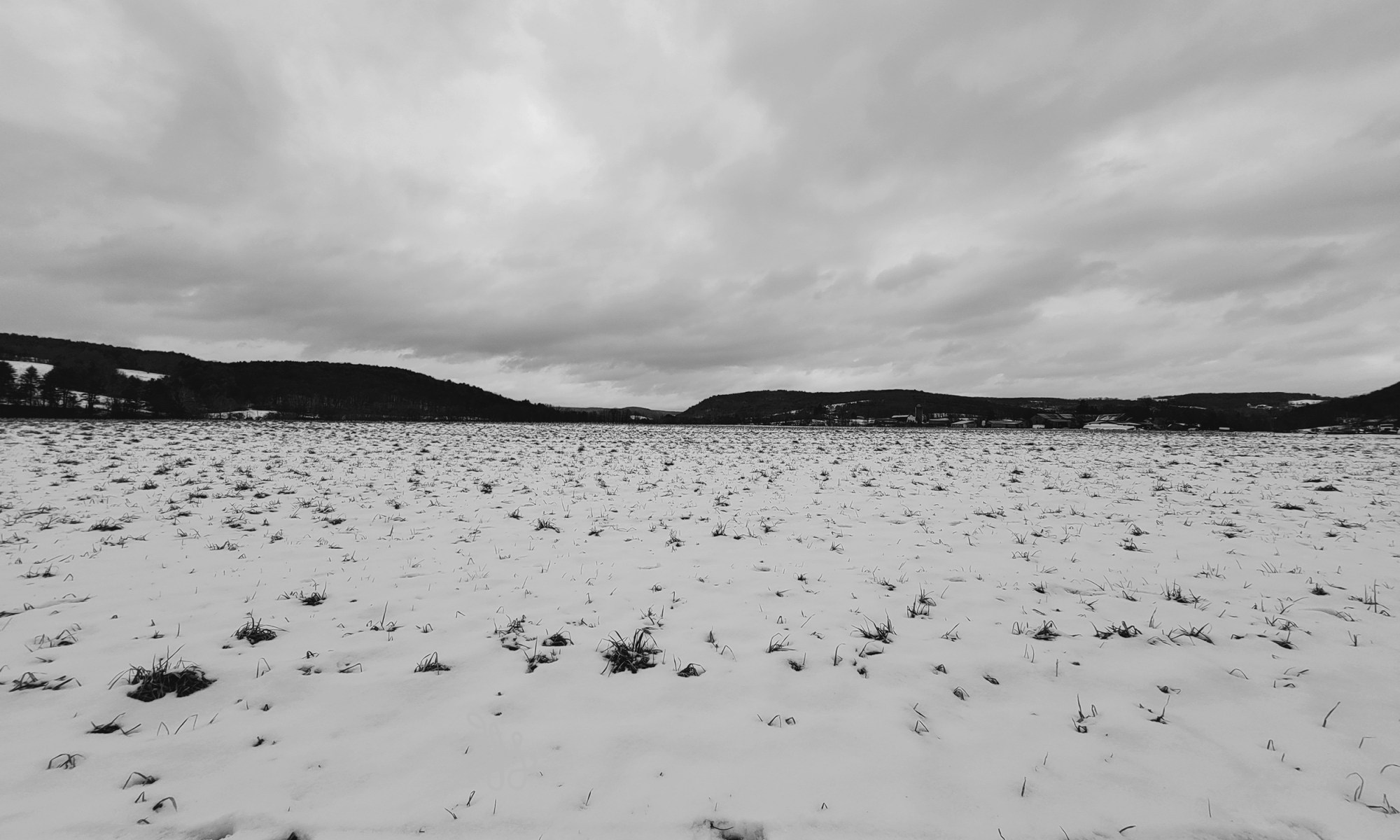 black and white of a stark landscape of field and sky with hills in distance